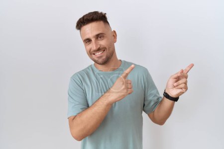 Photo for Hispanic man with beard standing over white background smiling and looking at the camera pointing with two hands and fingers to the side. - Royalty Free Image
