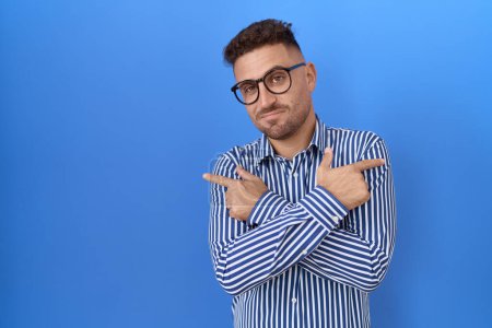 Foto de Hombre hispano con barba con gafas apuntando a ambos lados con los dedos, en diferente dirección en desacuerdo - Imagen libre de derechos