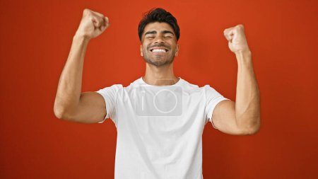Photo for Handsome young hispanic man celebrating triumphantly against a vibrant red background - Royalty Free Image