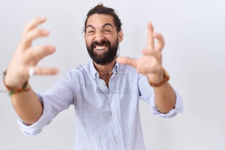 Photo for Hispanic man with beard wearing casual shirt shouting frustrated with rage, hands trying to strangle, yelling mad - Royalty Free Image