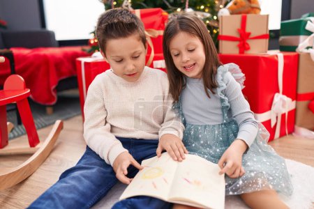 Photo for Adorable boy and girl reading book celebrating christmas at home - Royalty Free Image