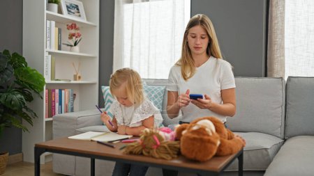 Photo for Relaxing at home, serious caucasian mother and daughter bonding over a drawing session on a notebook using their smartphone - Royalty Free Image