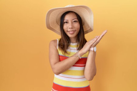 Téléchargez les photos : Femme chinoise du Moyen Âge portant un chapeau d'été sur fond jaune applaudissant et applaudissant heureux et joyeux, souriant mains fières ensemble - en image libre de droit