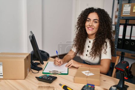 Foto de Young beautiful hispanic woman ecommerce business worker using laptop writing on document at office - Imagen libre de derechos