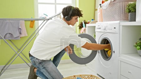 Foto de Guapo adolescente hispano joven rockea, absorto en la música, mientras aborda las tareas de lavandería en el cuarto de lavado de la casa - Imagen libre de derechos
