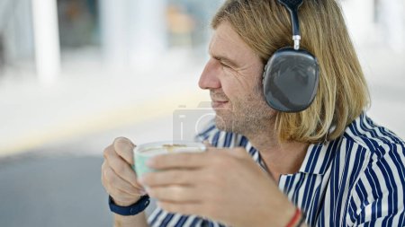 Foto de Un hombre sonriente con auriculares disfruta del café al aire libre en un moderno café urbano. - Imagen libre de derechos