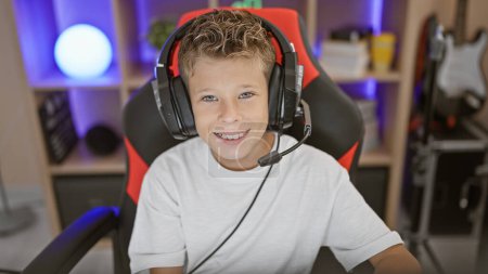 Photo for Adorable blond boy streamer happily playing gaming, streaming a video game on his computer at home in a futuristic gaming room, confidently using headset and gamepad - Royalty Free Image