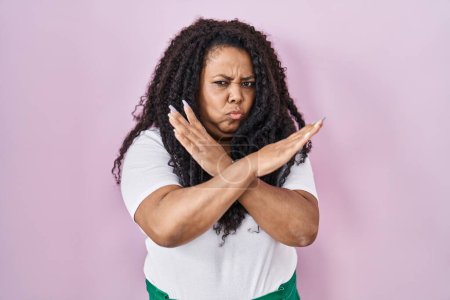 Foto de Más tamaño mujer hispana de pie sobre fondo rosa expresión de rechazo cruzando brazos haciendo signo negativo, cara enojada - Imagen libre de derechos