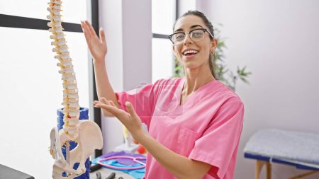 Téléchargez les photos : Une jeune physiothérapeute hispanique éclatante explique la santé de la colonne vertébrale avec un modèle anatomique à la clinique de réadaptation - en image libre de droit