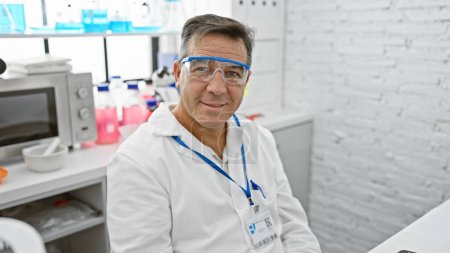 Photo for A mature male scientist with protective glasses poses in a well-equipped laboratory, showcasing research and healthcare professionalism. - Royalty Free Image