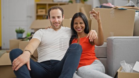 Photo for Beautiful couple sitting on floor together holding keys at new home - Royalty Free Image