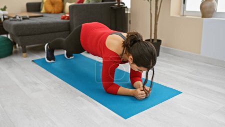 Téléchargez les photos : Une femme concentrée s'entraîne en position planche sur un tapis bleu dans un salon moderne, ce qui indique un mode de vie sain. - en image libre de droit