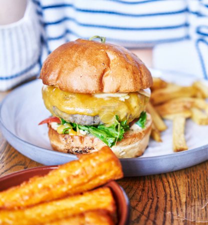 Téléchargez les photos : Plan rapproché d'un cheeseburger avec des frites et des pommes de terre hachées, présentant un délicieux repas sur une table en bois. - en image libre de droit