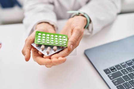 Téléchargez les photos : Young caucasian woman doctor holding birth control pills sitting on table at clinic - en image libre de droit
