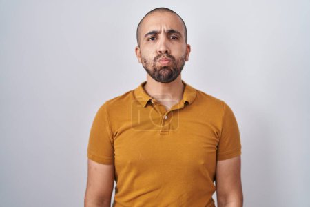 Photo for Hispanic man with beard standing over white background puffing cheeks with funny face. mouth inflated with air, crazy expression. - Royalty Free Image