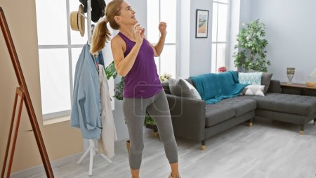 Foto de Mujer madura bailando alegremente en una acogedora sala de estar, mostrando vitalidad y felicidad. - Imagen libre de derechos