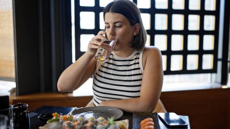 Foto de Joven mujer hispana hermosa comiendo sushi agua potable en el restaurante - Imagen libre de derechos