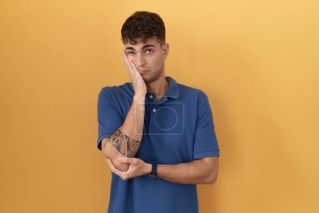 Photo for Young hispanic man standing over yellow background thinking looking tired and bored with depression problems with crossed arms. - Royalty Free Image