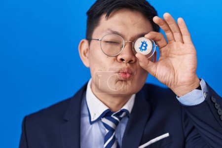 Photo for Young asian man holding virtual currency bitcoin covering eye looking at the camera blowing a kiss being lovely and sexy. love expression. - Royalty Free Image
