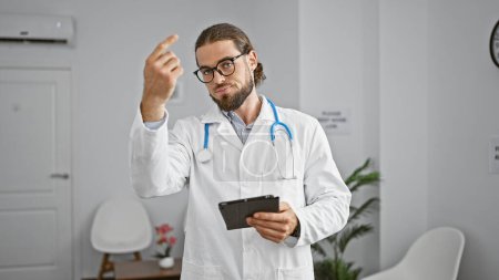 Téléchargez les photos : Jeune homme hispanique médecin utilisant pavé tactile demandant quelqu'un à la salle d'attente clinique - en image libre de droit
