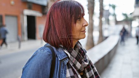 Photo for Mature hispanic woman in a denim jacket contemplates life on a bustling city street. - Royalty Free Image