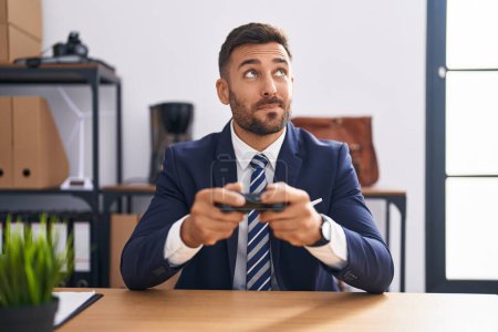 Photo for Handsome hispanic man playing video games at the office smiling looking to the side and staring away thinking. - Royalty Free Image
