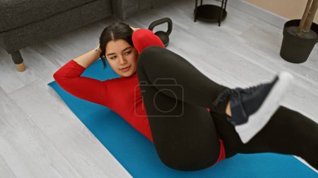 Téléchargez les photos : Jeune femme effectuant un entraînement abdominal sur tapis bleu à la maison. - en image libre de droit