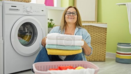 Photo for Middle age hispanic woman smiling confident holding folded towels at laundry room - Royalty Free Image