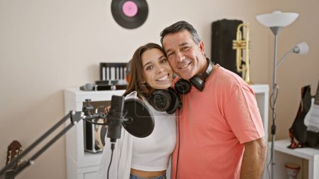 Foto de Músicos masculinos y femeninos confiados que usan auriculares, sonriendo juntos en el estudio de música mientras tocan un instrumento musical - Imagen libre de derechos