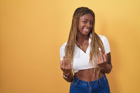 Photo for African american woman with braided hair standing over yellow background showing middle finger doing fuck you bad expression, provocation and rude attitude. screaming excited - Royalty Free Image