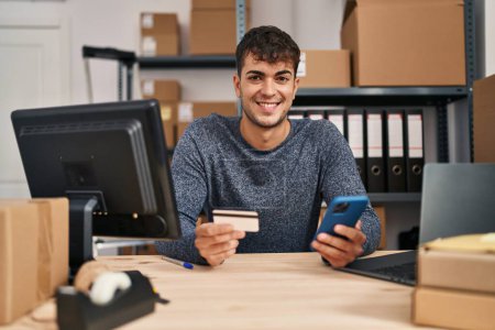 Téléchargez les photos : Jeune homme hispanique ecommerce travailleur d'affaires en utilisant smartphone et carte de crédit au bureau - en image libre de droit