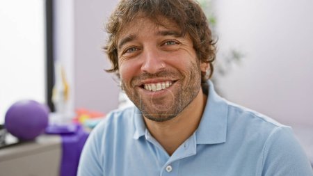 Foto de Retrato de un joven alegre con barba en una clínica, que transmite una sensación de bienestar y positividad. - Imagen libre de derechos