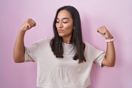 Téléchargez les photos : Young hispanic woman standing over pink background showing arms muscles smiling proud. fitness concept. - en image libre de droit