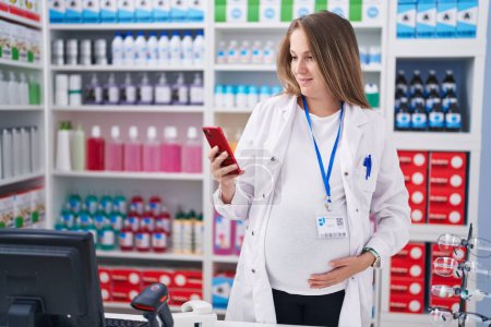 Photo for Young pregnant woman pharmacist using smartphone working at pharmacy - Royalty Free Image