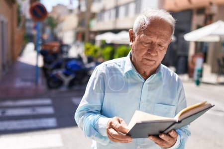 Photo for Middle age grey-haired man reading book at street - Royalty Free Image