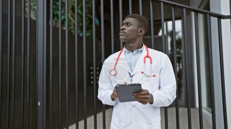 Téléchargez les photos : Africain homme médecin uniforme comprimé extérieur ville hôpital professionnel - en image libre de droit