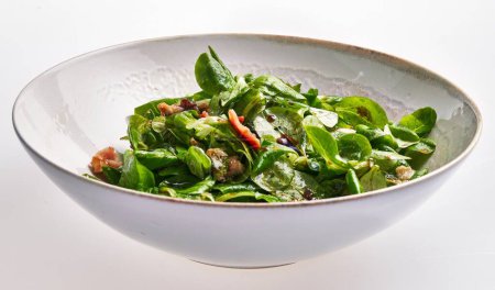 Photo for Fresh spinach salad with bacon, walnuts, and vinaigrette in a white bowl on a clean background. - Royalty Free Image