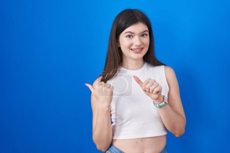 Photo for Young caucasian woman standing over blue background pointing to the back behind with hand and thumbs up, smiling confident - Royalty Free Image