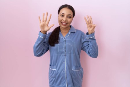 Foto de Mujer árabe joven con pijama azul mostrando y señalando hacia arriba con los dedos número ocho mientras sonríe confiado y feliz. - Imagen libre de derechos