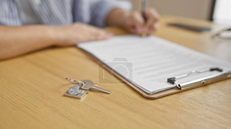 Foto de Un primer plano captura a un hombre firmando documentos junto a las llaves de la casa en un escritorio de madera, ilustrando un acuerdo inmobiliario. - Imagen libre de derechos