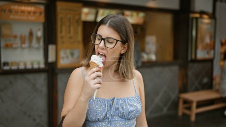 Photo for Cheerful hispanic woman savors deliciously sweet ice cream on kyoto street, her beautiful smile is framed by glasses while experiencing the traditional architecture of this japanese city - Royalty Free Image