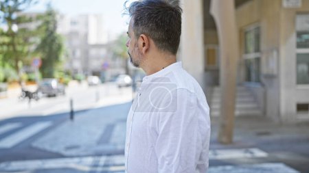 Téléchargez les photos : Jeune homme hispanique aux cheveux gris regardant du côté avec un visage sérieux dans la rue - en image libre de droit