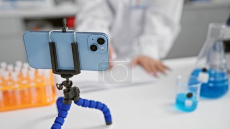 Photo for Female scientist's hands busy taking notes while engaging in a video call conversation in her laboratory, an indoor medical research centre, wearing her work uniform - Royalty Free Image