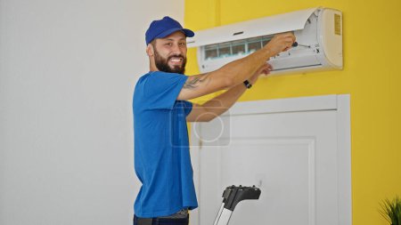 Téléchargez les photos : Jeune homme hispanique technicien réparer la machine de climatisation debout sur l'échelle à la maison - en image libre de droit