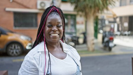 Téléchargez les photos : Belle femme afro-américaine exsudant confiance, riant joyeusement et profitant de la vie tout en se tenant tranquillement dans une rue urbaine, rayonnant de positivité et de joie. - en image libre de droit
