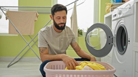 Téléchargez les photos : Jeune homme hispanique laver les vêtements à la buanderie - en image libre de droit