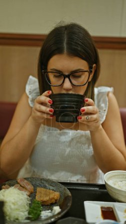 Foto de Impresionante mujer hispana disfruta de la sopa tradicional de miso en el restaurante asiático de moda, la opción perfecta de almuerzo saludable - Imagen libre de derechos