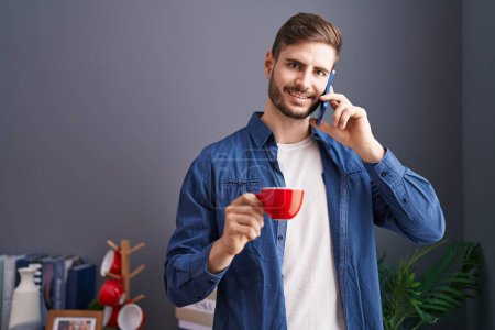 Foto de Young caucasian man talking on smartphone drinking coffee at home - Imagen libre de derechos
