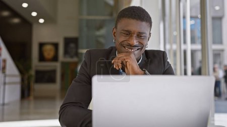 Photo for Smiling african man working on laptop in modern office indoor environment - Royalty Free Image