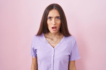 Photo for Young hispanic woman with long hair standing over pink background afraid and shocked with surprise and amazed expression, fear and excited face. - Royalty Free Image